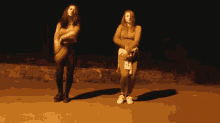two women are standing next to each other in a dark area