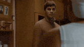 a man in a turtleneck sweater looks at another man in a white tank top