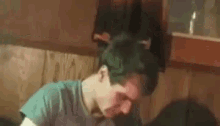 a man with green hair is sitting in a chair with his head on a table .
