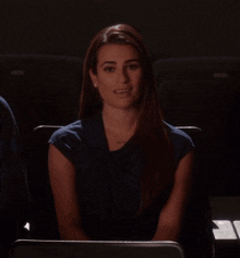 a woman sitting in a dark room with her eyes closed and her hands on her chest
