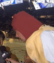 a man in a red hat is being interviewed by a snv reporter .