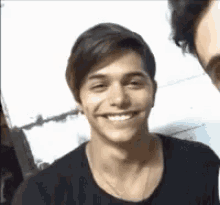 a young man in a black shirt is smiling while standing next to another young man .