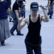 a man in a black tank top and hat is holding a microphone while a group of people are standing around him .