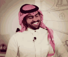 a man wearing a head scarf and a white shirt smiles for the camera