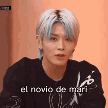 a young man with blue hair is wearing a black sweater and has the words el novio de mari written on his face .