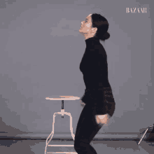 a woman in a black turtleneck is standing next to a white stool with the word bazaar on it