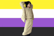 a woman in a sweater and skirt stands in front of a purple and yellow flag