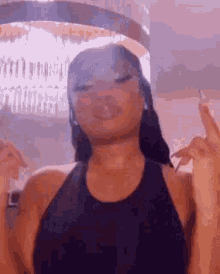 a woman in a black tank top is smoking a cigarette while giving the middle finger .