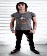 a young man wearing a mickey mouse t-shirt is standing with his hands in his pockets