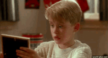 a young boy is looking at a picture frame with a woofmaker.com watermark on the bottom