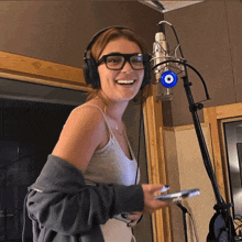 a woman wearing glasses and headphones stands in front of a microphone with a blue evil eye on it