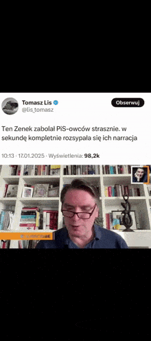a man wearing glasses is standing in front of a bookshelf ..