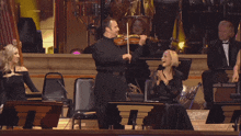 a man playing a violin in front of an orchestra with a woman clapping behind him
