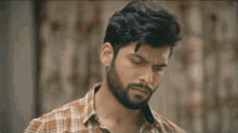 a man with a beard wearing a plaid shirt is looking to the side .