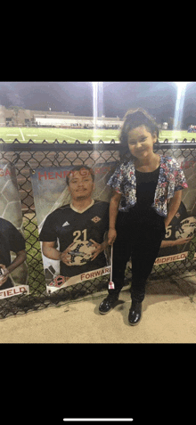 a little girl is standing in front of a fence with a picture of a soccer player with the number 21 on his jersey