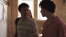 a man in a pink striped shirt talks to another man