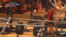 a woman in a red tank top runs through a fence while a scoreboard says titanes 8 5 heroes