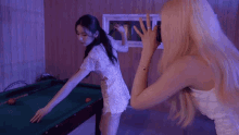 a woman taking a picture of a woman playing pool