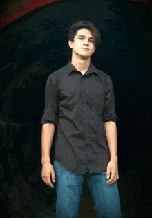 a young man wearing a black shirt and blue jeans is standing in front of a dark tunnel .