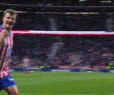 a man in a red and white striped shirt and blue shorts is playing soccer on a field .