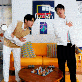two men standing in front of a yellow couch with a poster on the wall that says ' arcade '