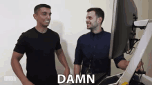 two men are standing next to each other in front of a computer and one of them is saying damn .