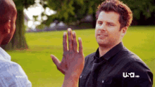 a man is giving another man a high five in a park .