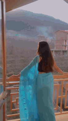 a woman in a blue saree is standing on a balcony overlooking a mountain .