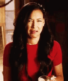 a woman in a red shirt is making a funny face while holding a glass of wine .