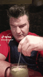 a man in a red shirt is drinking from a glass with a straw and a tiktok watermark