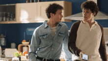 two men standing next to each other in a kitchen looking at a cell phone