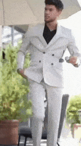 a man in a white suit and black shirt is holding an umbrella .