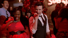 a man is singing into a microphone while a woman holds a red heart in her hand