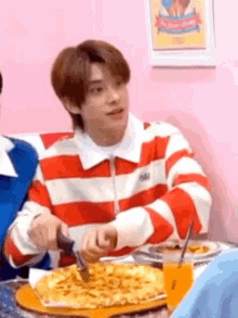 a man in a red and white striped shirt is cutting a pizza with a knife .