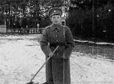 a black and white photo of a man in a military uniform holding a broom .