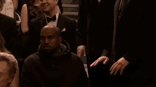 a man in a tuxedo is talking to a man in a black hoodie in a crowd .