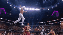 a wrestler is jumping over a rope while another wrestler looks on