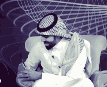 a man wearing a hat and a scarf sits in a chair with a pen in his hand