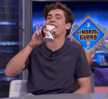 a young man is drinking from a mug in front of a sign that says el hormiguero