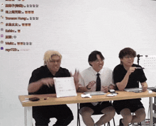 three men sitting at a table with chinese writing on the wall
