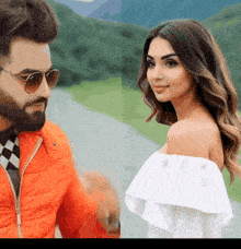 a man in an orange jacket and a woman in a white off the shoulder top are standing next to each other
