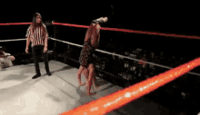 a referee is standing in a wrestling ring watching a wrestler throw another wrestler .