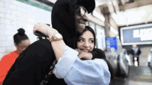 a man in a black hoodie hugging a woman in a blue shirt