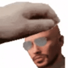 a hand is holding a man 's head with a beard and sunglasses .