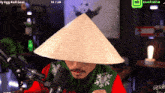 a man wearing a conical hat is sitting in front of a microphone in a room