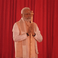 a man with a beard is standing in front of a red curtain holding a cane