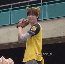 a young man in a yellow baseball uniform is holding a baseball glove and smiling .