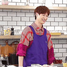 a man wearing a purple apron is smiling in a kitchen