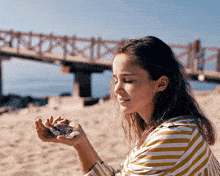 a woman in a striped shirt is holding sand in her hands on the beach