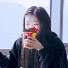 a woman is holding a cup of food with a chinese symbol on the front